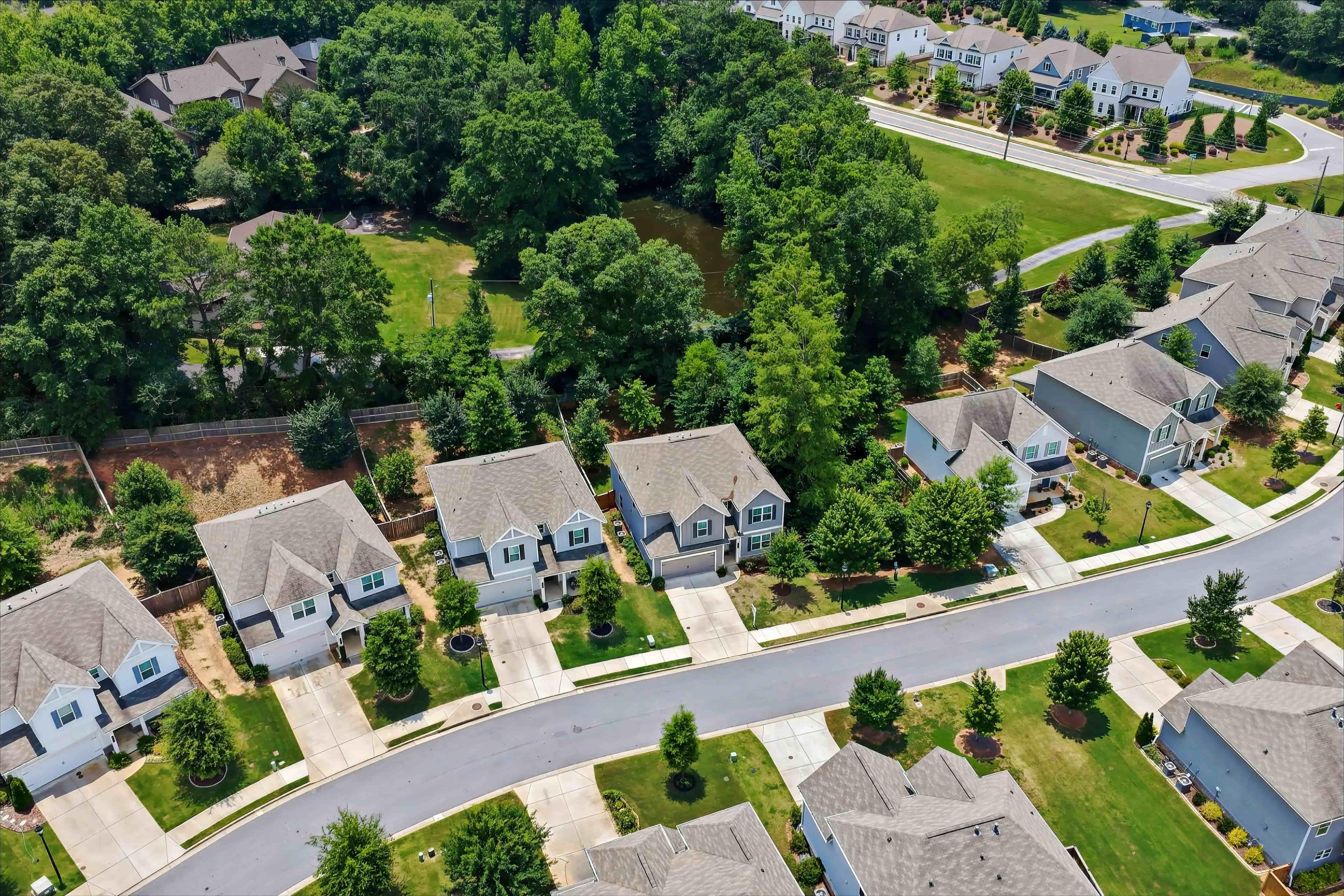 Aerial view of a suburban neighborhood with two-story homes, mature trees, and a wooded pond area